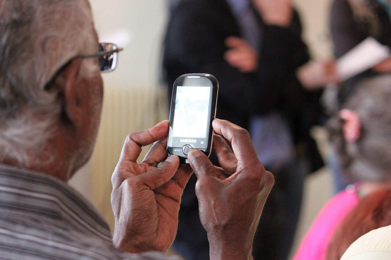 Un bărbat mai în vârstă care se uită la un telefon mobil.